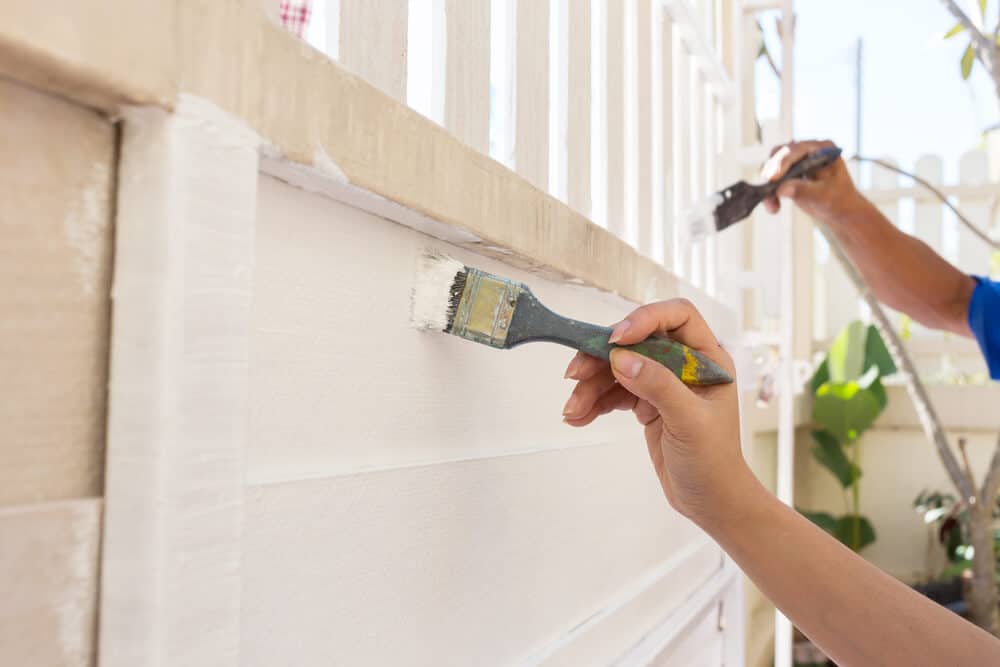 Hand worker holding brush painting white on wood - Golden Gate Fences